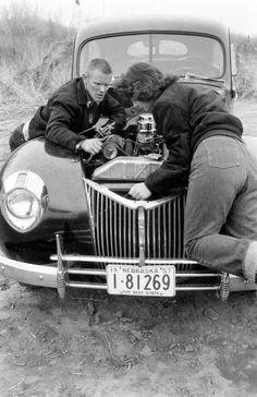 two men leaning on the hood of an old car