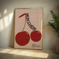 a framed poster with two cherries on it next to a potted plant