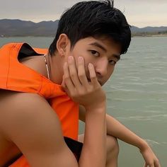 a boy in an orange life jacket sitting on the back of a boat with his hands to his face