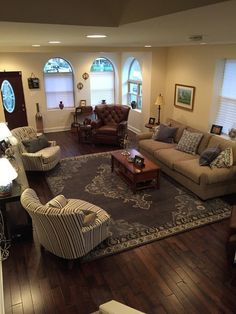 a living room filled with lots of furniture next to two windows and a rug on the floor