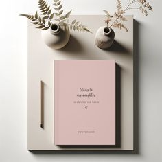 a pink book sitting on top of a table next to two vases and a pen