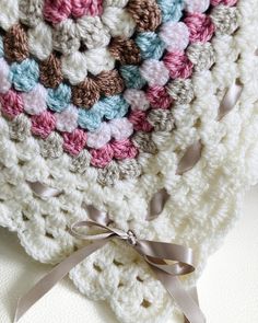 a crocheted blanket with a bow on the end and ribbon around it,