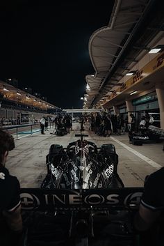 a race car is parked in front of the pit area at night with people standing around it