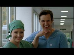 a man in scrubs standing next to a smiling woman wearing a green head wrap