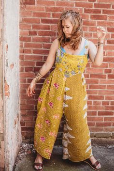 a woman standing in front of a brick wall wearing a yellow and white jumpsuit