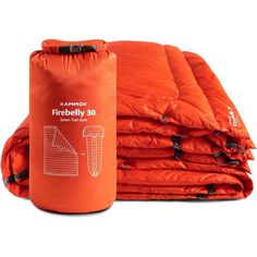 an orange sleeping bag next to a pile of folded down blankets on a white background