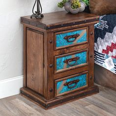 a wooden cabinet with three drawers on top of it next to a quilt and potted plant