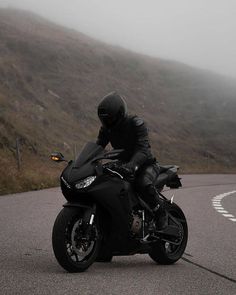 a man riding on the back of a black motorcycle down a curvy road