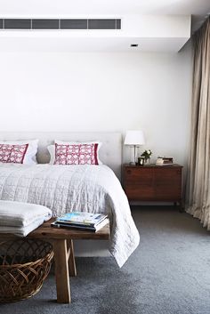 a white bed sitting next to a window with curtains on top of it and a wooden coffee table in front of it