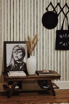 a wooden table topped with a white vase next to a black and white striped wall