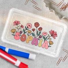 a clear plastic case with flowers and the word sopho on it next to two markers