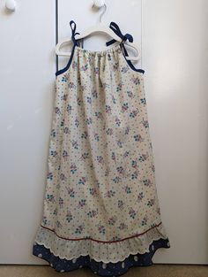 "Your child will feel cool and comfortable all summer long in this loose fitting sundress with adjustable tie straps. This dress features a small patch pocket on the front of the dress, a ruffled hem, and a lovely navy and cream floral pattern. This dress is fully lined, as the main fabric is very lightweight. This listing is for the navy and cream sundress as shown in the thumbnail. The blue check dress on the model is only to show the fit of the dress. This dress is listed as size 5-7, but ple Cotton Sundress With Tie And Ruffled Straps, Vacation Cotton Sundress With Ruffled Straps, Cotton Sundress With Ruffled Straps For Vacation, Cotton Sundress With Ruffle Hem, Cotton Sundress With Ruffled Straps, Summer Cotton Sundress With Ruffled Straps, Cotton Sundress With Tie Back And Ruffled Straps, Casual Cotton Sundress With Ruffled Straps, Cute Sundress With Ruffled Adjustable Straps