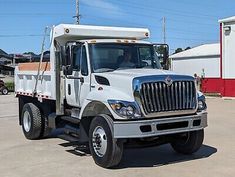 a white dump truck parked in a parking lot next to a red and white building