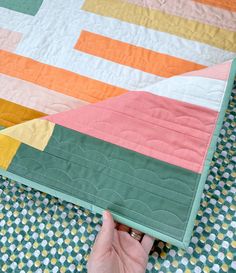 a person is holding up a quilt on the ground with their hand in front of it