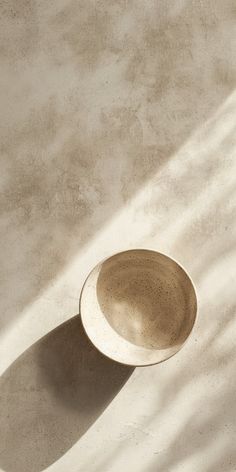 a white bowl sitting on top of a cement floor next to a shadow cast wall