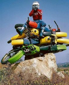 a man riding on the back of a yellow and blue motorcycle down a rocky hill