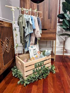 a wooden crate filled with baby clothes on top of a hard wood floor next to a coat rack