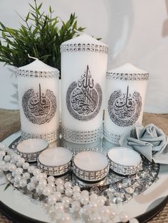 three white candles sitting on top of a plate next to pearls and flowers in front of a plant