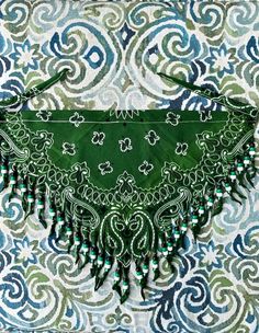 a green purse sitting on top of a blue and white patterned table cloth with beads hanging from it's sides