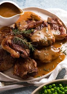 a white plate topped with meat covered in gravy next to peas and sauce