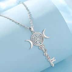 a silver necklace with a key and crescents on it, sitting on top of a blue