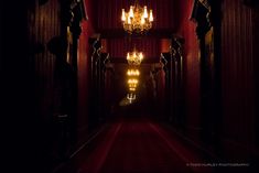 an empty hallway with chandeliers and red walls in the dark, at night