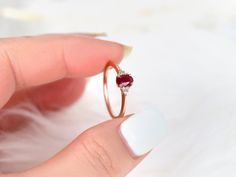 a woman's hand holding an engagement ring with a red stone in the middle