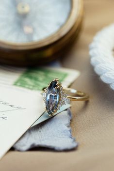 an engagement ring sitting on top of a piece of paper next to a pocket watch