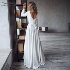 a woman in a long white dress is leaning against a book shelf with her back to the camera