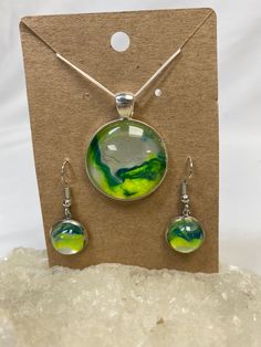 Thank you for your interest in this acrylic painted pendant necklace and earring set that was created using a liquid paint pouring technique. They're handmade acrylic paint "skins" set into bezel trays, all topped with glass cabochons. Both the 1-inch pendant and the 1/2-inch earrings are round. The pendant will be attached to your choice of an 18" waxed cotton necklace cord plus a 2-inch chain extender available in 7 different colors (please see the picture) or a keychain available in 2 differe Artistic Nickel-free Resin Jewelry, Artsy Round Green Jewelry, Round Large Pendant Jewelry In Resin, Artistic Green Cabochon Jewelry, Artistic Green Jewelry With Cabochon, Green Hand Painted Round Pendant Jewelry, Artistic Resin Jewelry, Acrylic Paint Pour, Cotton Necklace