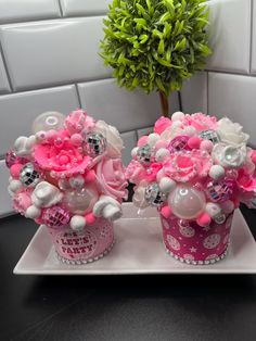 two pink and white cupcakes with flowers in them on a plate next to a potted plant