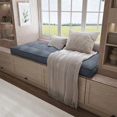 a window seat with pillows and blankets on it in front of a book shelf filled with books