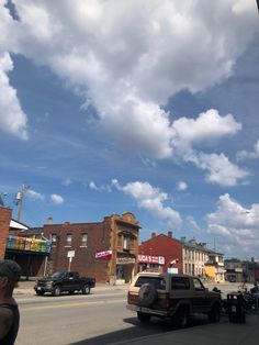 cars are parked on the side of the road near buildings and clouds in the sky