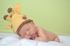 a baby wearing a crocheted giraffe hat laying on top of a bed