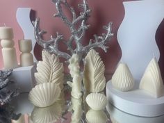 some white candles are sitting on a table next to shells and seaweed, with other decorations in the background