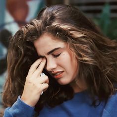 a young woman holding her hand to her ear and looking down at the ground while she holds