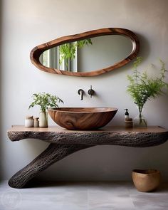 a bathroom sink sitting under a mirror next to a wooden table with potted plants on it