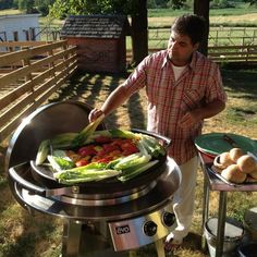 a man standing next to a bbq grill with vegetables on it