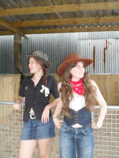 two young women standing next to each other in front of a metal fence wearing cowboy hats