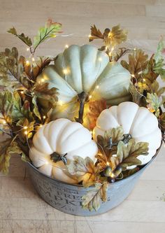 a bucket filled with white pumpkins and greenery on top of a wooden floor