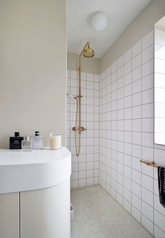 a white tiled bathroom with gold fixtures and an open shower head, along with two candles on the counter