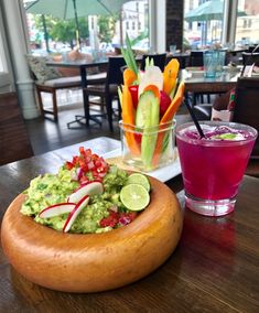 a wooden bowl filled with guacamole next to a glass of pink juice