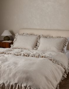 a bed with white linens and ruffled pillows