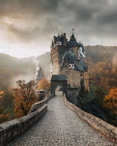 an old castle on top of a hill in the middle of trees and foggy sky