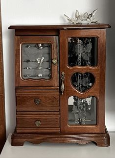 a wooden cabinet with glass doors and drawers on the bottom, in front of a white wall