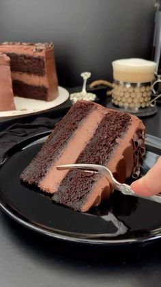 a slice of chocolate cake on a black plate with a hand holding a fork in front of it