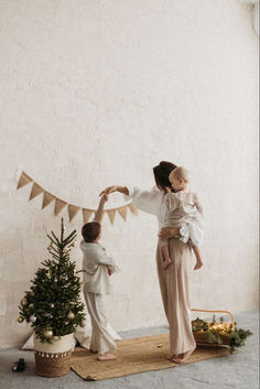 a woman holding a baby in her arms while standing next to a small christmas tree