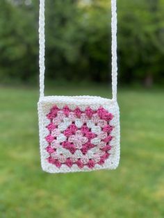 a crocheted square hanging from a string in front of some grass and trees