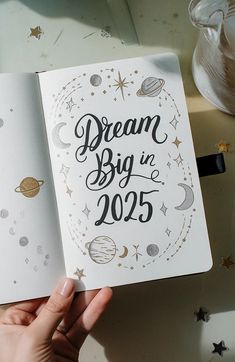 a hand holding an open notebook with the words dream big in 205