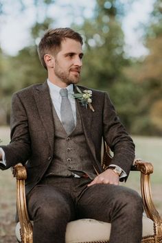 a man sitting in a chair wearing a suit and tie with a boutonniere on his lapel